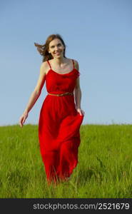 Young beautiful woman with a red dress walking on a green meadow