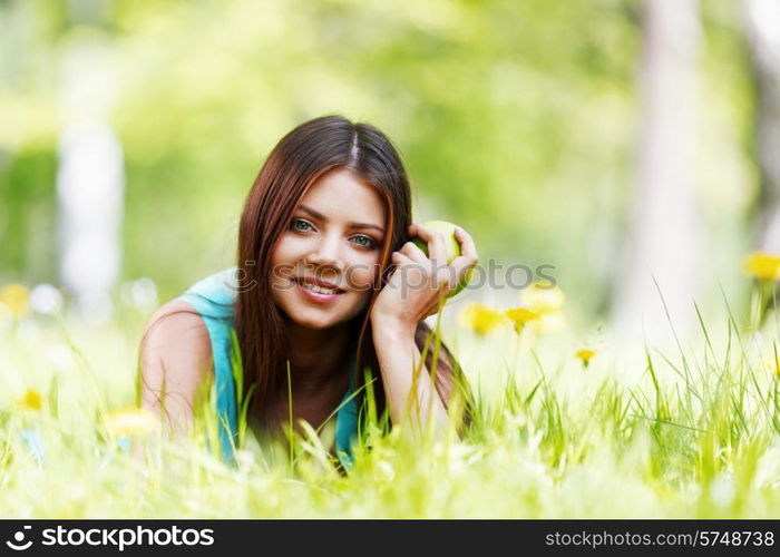 Young beautiful woman with apple resting on fresh green grass with flowers