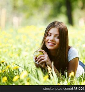 Young beautiful woman with apple resting on fresh green grass with flowers