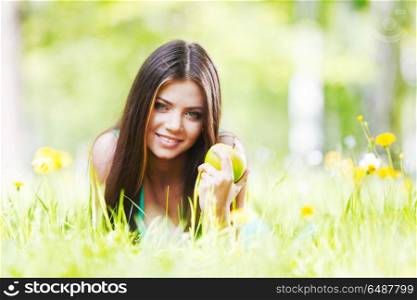 Young beautiful woman with apple resting on fresh green grass with flowers. Woman on flower field