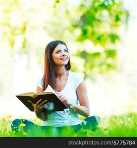 Young beautiful woman with book resting on fresh green grass with flowers. Woman on flower field