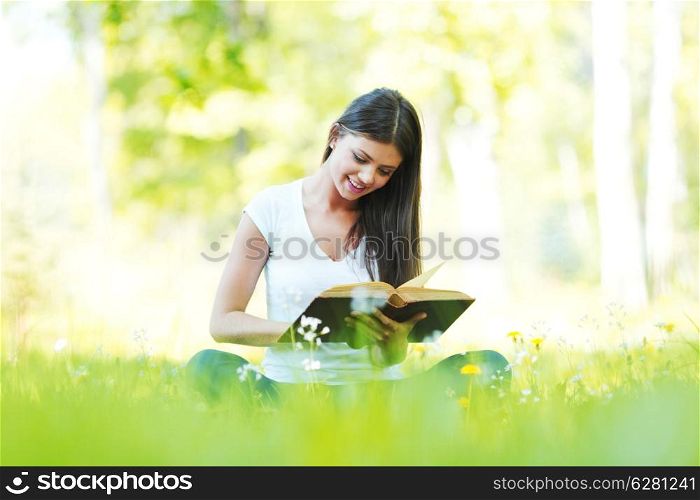 Young beautiful woman with book resting on fresh green grass with flowers