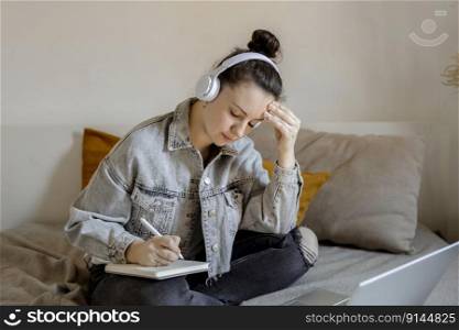Young beautiful woman with casual clothes sitting on the bed at home with laptop computer and studying. Girl is sad and tired. Negative emotions, stress, mental problems, deadline. Distance education. Young beautiful woman with casual clothes sitting on the bed at home with laptop computer and studying. Girl is sad and tired. Negative emotions, stress, mental problems, deadline. Distance education.