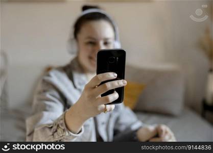 Young beautiful woman with casual clothes sitting on the bed at home and making selfie on smartphone. Girl using mobile phone to surf in internet, make video call, talk with friends. Influencer. Young beautiful woman with casual clothes sitting on the bed at home and making selfie on smartphone. Girl using mobile phone to surf in internet, make video call, talk with friends. Influencer.