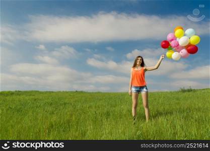 Young beautiful woman with colorful balloons on a green meadow