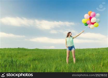 Young beautiful woman with colorful balloons on a green meadow