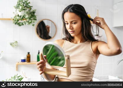 Young beautiful woman with dark skin looking into face mirror. Wellness, self-care concept. Young beautiful woman with dark skin looking into face mirror