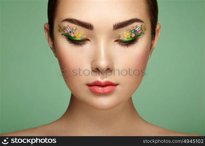 Young beautiful woman with flower makeup eyes. Spring makeup. Beauty fashion. Eyelashes. Cosmetic Eyeshadow. Make-up detail. Girl on green background