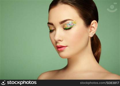Young beautiful woman with flower makeup eyes. Spring makeup. Beauty fashion. Eyelashes. Cosmetic Eyeshadow. Make-up detail. Girl on green background