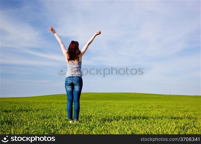 Young beautiful woman with hands up on green sunny field