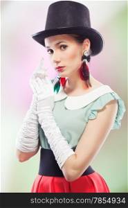 Young beautiful woman with red glamour lips and eye arrow make-up wearing fancy plastic earrings, top hat and white formal gloves, on coloured background, retro beauty style