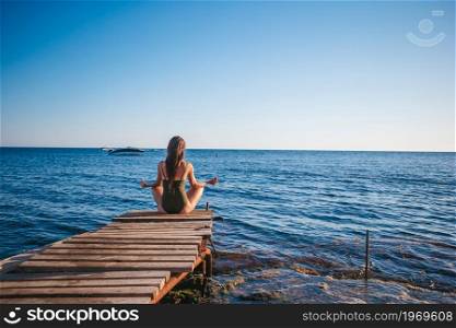 Young beautiful woman woman practicing yoga on the pier. Young beautiful woman on yoga on the beach