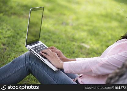Young beautiful woman working outdoor in a public park. Working on laptop outdoors. Cropped image of female working on laptop while sitting in a park.