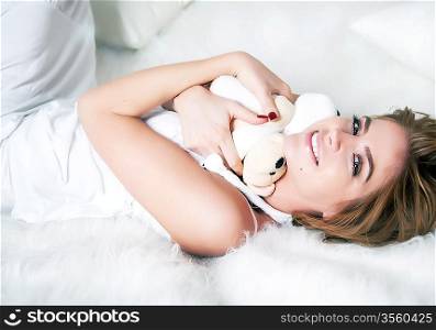 Young beauty female laying in white bed with soft toy - teddy bear. Saint Valentine&acute;s day (or birthday)