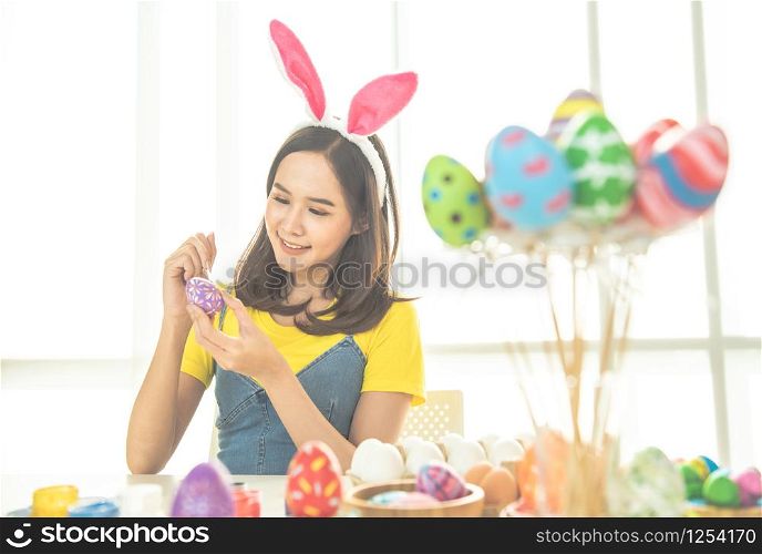Young beauty happy asian woman wearing bunny ears handmade painting on colorful Easter egg by art design paintbrush with decorative style.