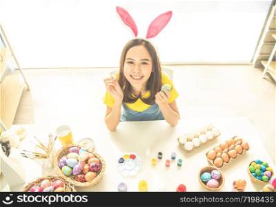 Young beauty happy asian woman wearing bunny ears handmade painting on colorful Easter egg by art design paintbrush with decorative style.