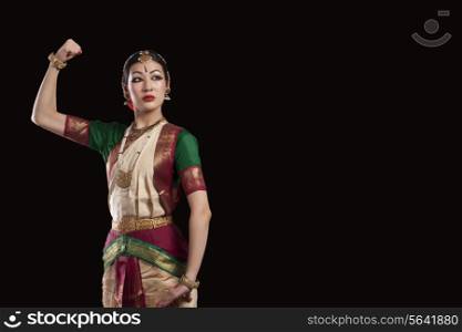 Young Bharatanatyam dancer flexing muscle over black background