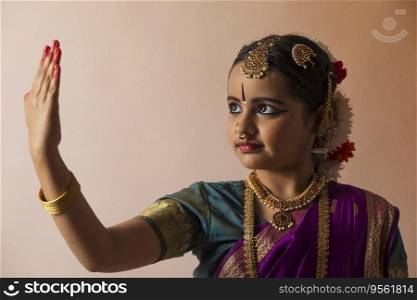 Young bharatnatyam dancer gracefully looking at her palm in front of a plain background. 