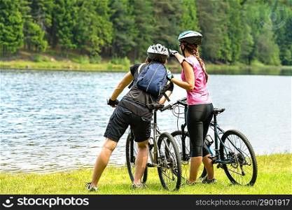 Young bikers standing at lake watching the forest
