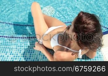Young bikini woman sunbathing by swimming pool
