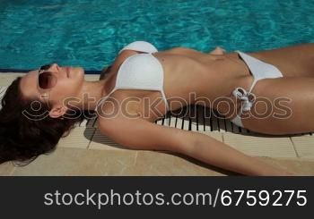 Young bikini woman sunbathing by swimming pool