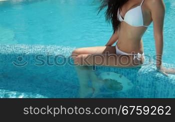 Young bikini woman sunbathing by swimming pool, obscured face