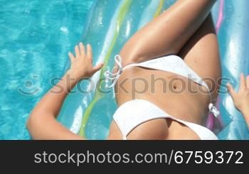 Young bikini woman sunbathing on air bed in pool