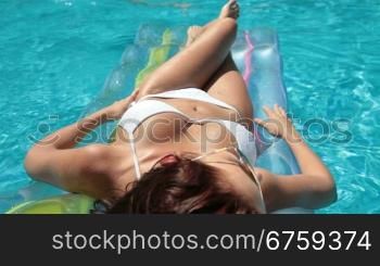 Young bikini woman sunbathing on air bed in pool