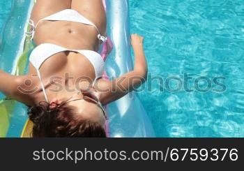 Young bikini woman sunbathing on lilo in pool