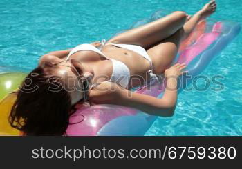 Young bikini woman sunbathing on lilo in swimming pool