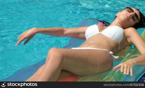 Young bikini woman sunbathing on pool raft in pool