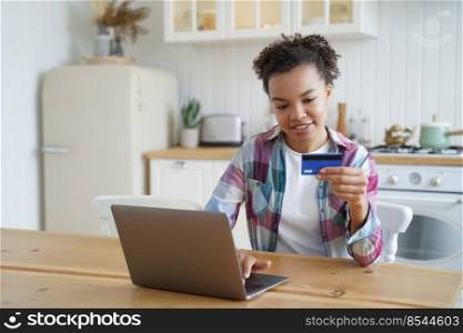 Young biracial girl ecommerce client using bank card to make electronic payment online via app on laptop. Smiling mixed race woman shopping online on computer uses banking system service.. Young biracial girl ecommerce client using banking credit card to pay online on laptop at home