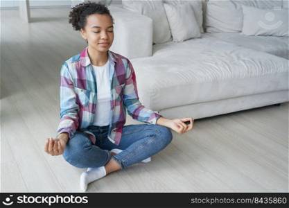 Young biracial girl practice yoga, sitting in padmasana lotus pose while meditation. Eyes closed african american woman meditate with mudra gesture on floor at home. Healthy lifestyle, wellness.. African american young girl practice yoga, meditate on floor at home. Healthy lifestyle, wellness