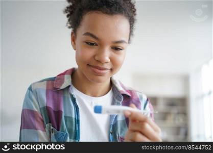 Young biracial girl using digital thermometer happy with her body temperature. Smiling african american woman checking temp before trip during coronavirus covid pandemic.. Young biracial girl uses digital thermometer happy with body temperature during coronavirus pandemic