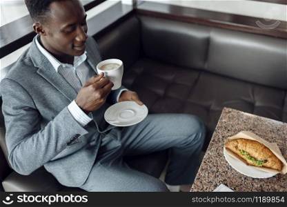Young black businessman having lunch in office cafe. Successful business person drinks coffee in food-court, black man in formal wear. Black businessman having lunch in office cafe
