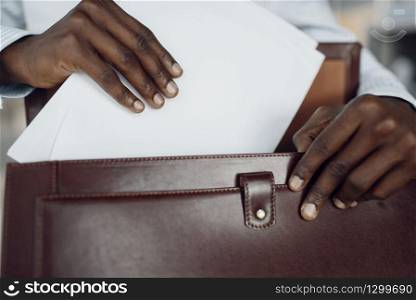 Young black businessman holds briefcase in car showroom. Successful business person on motor show, black man in formal wear. Black businessman holds briefcase in car showroom