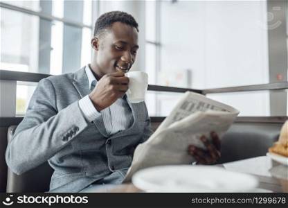 Young black businessman with newspaper having lunch in office cafe. Successful business person drinks coffee in food-court, black man in formal wear. Black businessman having lunch in office cafe