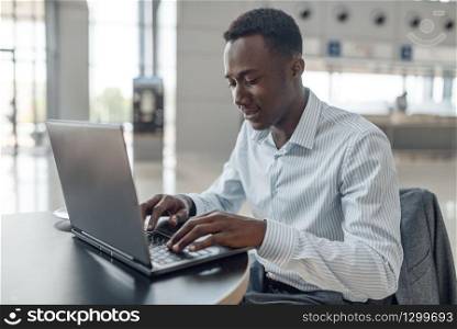 Young black businessman working on laptop in car showroom. Successful business person on motor show, black man in formal wear. Businessman working on laptop in car showroom