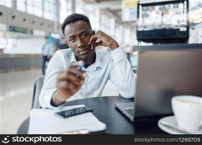 Young black businessman working on laptop in office cafe. Successful business person drinks coffee in food-court, black man in formal wear. Black businessman working on laptop in office cafe