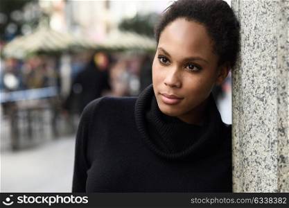 Young black female standing in an urban street. Mixed woman wearing poloneck sweater and skirt.