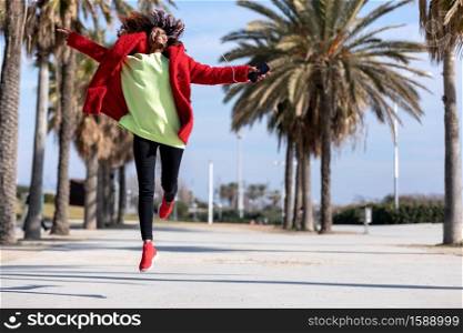 Young black girl with afro hairstyle jumping in urban background.