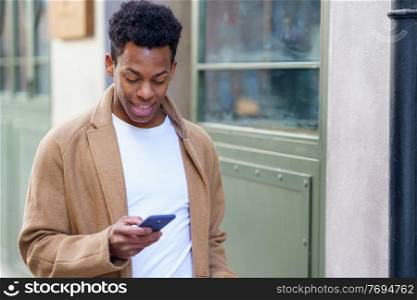 Young black man consulting his phone while walking down the street. Cuban guy in urban background.. Young black man consulting his phone while walking down the street.