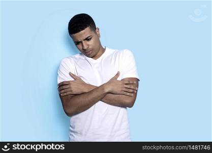 Young black man isolated on blue background while arms crossed and looking down pensive