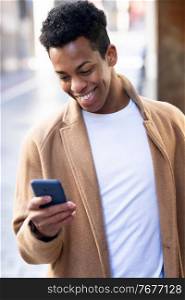 Young black man using his smartphone outdoors. Cuban guy smiling in urban background.. Young black man using his smartphone outdoors.