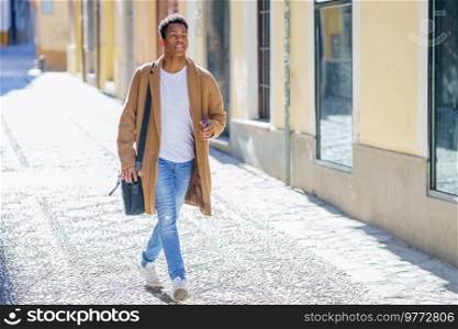 Young black man walking down the street carrying a briefcase and a smartphone. Cuban guy in urban background.. Young black man walking down the street carrying a briefcase and a smartphone.
