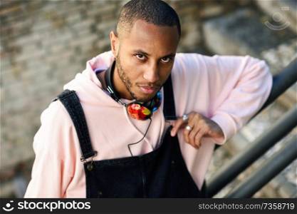 Young black man wearing casual clothes on urban steps. Serious African guy with bib pants outdoors. Serious African guy with bib pants outdoors