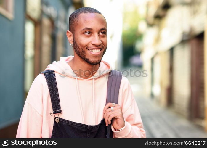 Young black man wearing casual clothes walking smiling down the street. Millennial african guy with bib pants outdoors