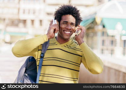 Young Black man with afro hairstyle listening to music with wireless headphones sightseeing in Granada, Andalusia, Spain.. Black man listening to music with wireless headphones sightseeing in Granada