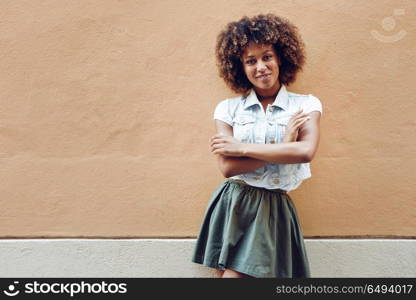 Young black woman, afro hairstyle, smiling in urban background. Young black woman, afro hairstyle, smiling near a wall in the street. Girl wearing casual clothes in urban background.