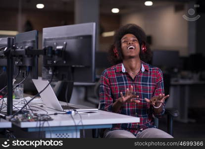 young black woman at her workplace in startup business office listening music on headphones and playing music instruments while relaxing